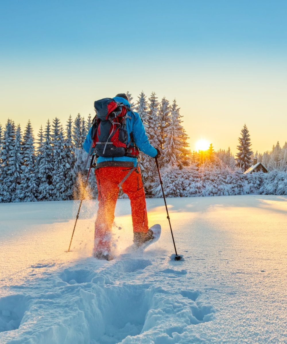 Snowshoe walker running in powder snow with beautiful sunrise light. Outdoor winter activity and healthy lifestyle